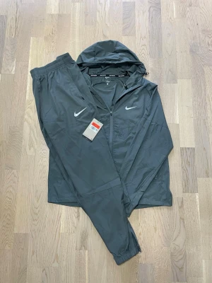 Stilrent Nike tracksuit set i snygg grå färg ⚡️ - Ett lätt och sportigt set med jacka och byxor som matchar perfekt. Reflekterande Nike-loggor ger både stil och synlighet. Perfekt för träning eller en clean streetwear-look. Kommer med tags.  • Märke: Nike   • Typ: Tracksuit set (jacka + byxor)   • Färg: Grå   • Passform: Regular fit M/S • Skick: Ny med tags   • Lätt och bekvämt material, perfekt för sommar! • Reflekterande detaljer    Perfekt både för träning och vardag. Ett riktigt snyggt och användbart set.