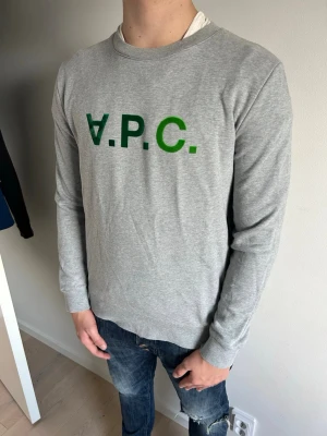 Grå sweatshirt från A.P.C. - Snygg grå sweatshirt från A.P.C. med grönt tryck på bröstet. Riktigt trendig tröja just nu och passar till i princip allting. Tveka inte på att höra av er vid frågor, vi svarar inom kortast möjliga tid!