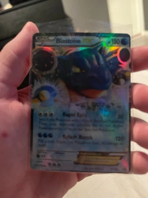 Blastoise EX Pokémonkort - Säljer ett Blastoise EX Pokémonkort med holografisk yta. Kortet har färgstarka detaljer och visar Blastoise i en kraftfull pose. Perfekt för samlare eller Pokémonfans som vill utöka sin kortsamling.