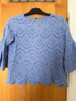  blus med halvklart ärm  -  blå blus med broderade hålmönster och vågig kant nertill. Blusen har halvkort ärm och en liten knapp i nacken. Barn storlek! Storleksetiketten blev avklippt,128-137  