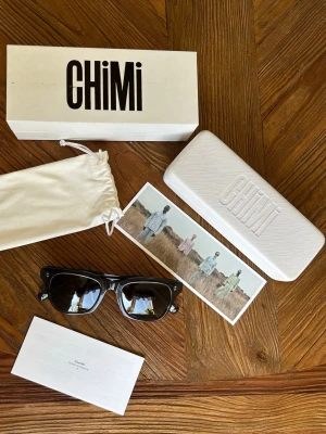 Svarta solglasögon från Chimi - Snygga svarta solglasögon från Chimi med klassisk, fyrkantig form. Bågarna är i blank svart plast och glasen är mörka. Kommer med originalväska, box och putsduk. Perfekta för dig som vill ha en stilren och modern look.