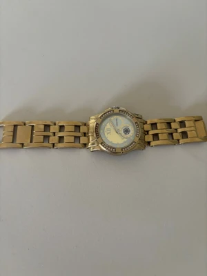 Guldfärgad klocka - Snygg guldfärgad klocka från Michael Kors med länkarmband i metall. Urtavlan är dekorerad med gnistrande stenar runt kanten och har en ljus bakgrund med romerska siffror och en extra liten urtavla.