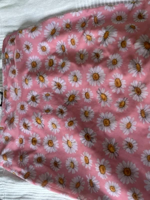 Rosa blommig kortkjol från Monki - Supersöt rosa kortkjol från Monki med ett härligt blommigt mönster av vita prästkragar. Kjolen har en mjuk och lätt känsla, perfekt för soliga dagar. Passar dig som vill ha en färgglad och lekfull stil.