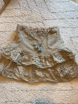 Grön  volangkjol med broderi - Supersöt grön kortkjol med volanger och broderade detaljer. Kjolen har knytband med tofsar framtill. Perfekt för sommarens alla tillfällen.