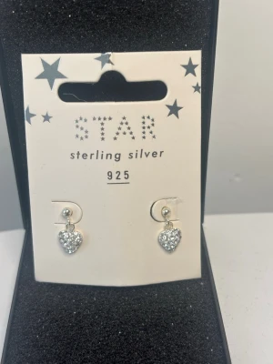 Silverörhängen med hjärtan från STAR - Säljer ett par söta örhängen från STAR i äkta sterling silver 925. Örhängena har gnistrande hjärtan med små glittriga stenar som ger en lyxig känsla. Perfekta för dig som gillar stilrena och eleganta accessoarer.