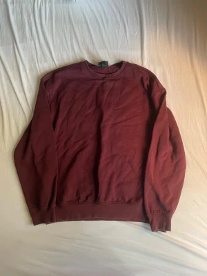 Vinröd sweatshirt utan huva - En enkel och stilren vinröd sweatshirt i mjukt bomullsmaterial. Tröjan har rund halsringning, långa ärmar och ribbade muddar vid ärmslut och nederkant. Perfekt för en avslappnad look och lätt att matcha med jeans eller joggers.
