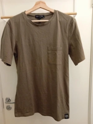 Olivgrön t-shirt från Lofty Manner - Snygg olivgrön t-shirt från Lofty Manner med rund halsringning och en bröstficka. T-shirten har en enkel och clean design, perfekt till jeans eller shorts. Tillverkad i mjuk bomull för skön känsla hela dagen.