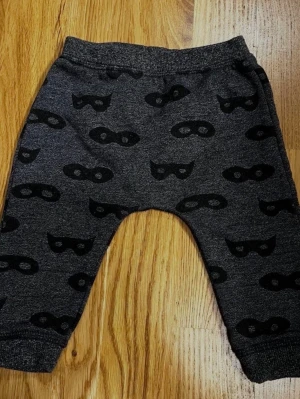Grå / svarta barn / baby byxor från H&M - Storlek 62 - Ett par fina babybyxor i grått med lekfullt mönster av svarta masker! Byxorna har resår i midjan och muddar vid anklarna, för en bra passform! Perfekta för både vardag och lek! Material: 60% Bomull och 40% Polyester. Storlek: 62 (2–4 månader) Varumärke: H&M. Säljs i mycket bra skick! Kika gärna in på mina andra annonser, jag säljer flera barnplagg!