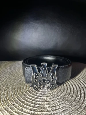 Svart skärp med stor silverdetalj - Snyggt svart bälte i skinn med en stor, iögonfallande silverfärgad logotyp som spänne. Perfekt accessoar för att lyfta din outfit och ge en edgy vibe. Bältet har en klassisk design med modern twist tack vare det unika metallspännet.