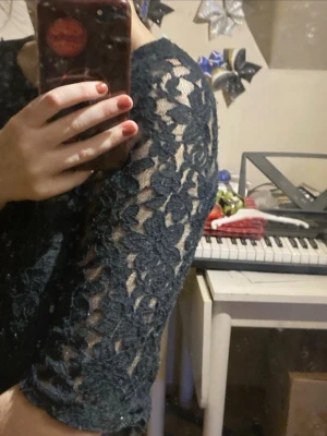 Svart croppad spetsblus - Säljer en svart croppad blus med blommigt spetsmönster och trekvartsärm. Toppen har en snygg transparent look på ärmarna och är perfekt för dig som gillar trendiga detaljer. Passar till många olika stilar. Lappen är borta men uppskattar storleken som xxs. I använt skick och lite nopprig men inga större defekter.