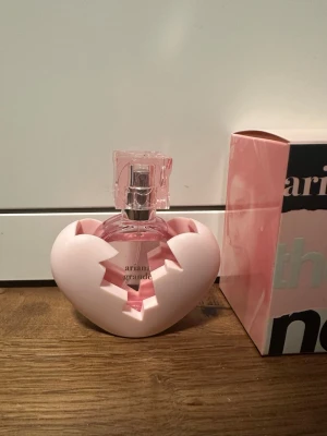 Ariana Grande Thank U Next parfym - Ariana Grande Thank U Next parfym i en unik rosa flaska med ett trasigt hjärta som hölje. Flaskan är rund och har ett fyrkantigt lock i genomskinlig rosa plast. Förpackningen är rosa och svart med modern textdesign. Aldrig använt, orginal pris 595kr.
