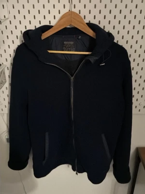  Woolrich cardigan - Mörkblå hoodie från Woolrich Teton med hel dragkedja framtill och två fickor. Jackan har huva och en stilren design som passar perfekt till lager-på-lager. Märkeslapp på insidan och mjukt material.
