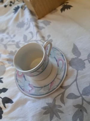 Kaffekopp med fat, pastellmönster - Säljer ett servis-set bestående av 6 koppar och 6 fat i porslin med ett stilrent blommönster i dämpade färger. Perfekt för dig som vill komplettera din servis eller ha fina koppar till kaffe eller  - 6 koppar och 6 fat - Material: Porslin - Mönster: Blommönster i ljusa pastellfärger - I gott skick utan synliga skador eller nagg - Kakfatens undersida märkt med tillverkarens stämpel (se bild) - Passar både vardagsbruk och festliga tillfällen Setet säljs komplett som en helhet.