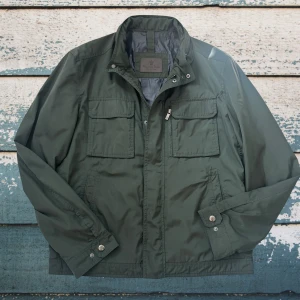 Mörkgrön vindjacka från Massimodutti  - Stilren mörkgrön vindjacka från Massimodutti med fyra framfickor, dragkedja och tryckknappar. Jackan har hög krage och är tillverkad i ett lätt, vattenavvisande material. Perfekt för blåsiga dagar och enkel att matcha med olika outfits.