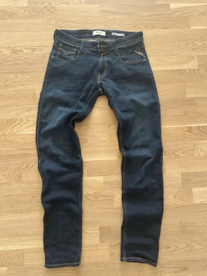 Mörkblå jeans från Replay - Säljer ett par mörkblå jeans från Replay med klassisk femficksdesign och kontrastsömmar. Jeansen har en smal passform och är tillverkade i stretchigt denimtyg för extra komfort. Perfekta för dig som gillar en stilren och tidlös look. Använda påriktigt max 5 gånger. Kan gå ner i pris vid snabb affär!