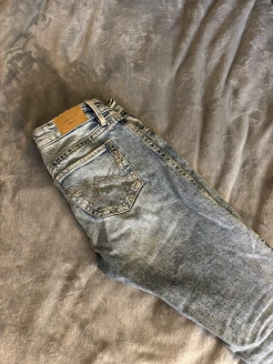 Ljusblå bootcut jeans från Wrangler - Säljer ett par ljusblå bootcut jeans från Wrangler med klassisk femficksdesign och snygga kontrastsömmar på bakfickan. Jeansen har en avslappnad passform och är tillverkade i slitstarkt denimtyg. Perfekta för en casual look.