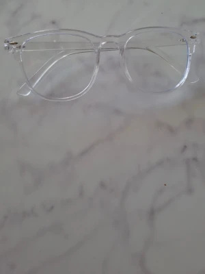 Transparenta solglasögon med klar båge - Snygga solglasögon med transparent båge och klassisk form. Glasögonen har en stilren och modern look som passar perfekt till alla outfits. Bågen är gjord i syntetmaterial och har en lätt känsla. Perfekt accessoar för dig som vill sticka ut med en clean stil.