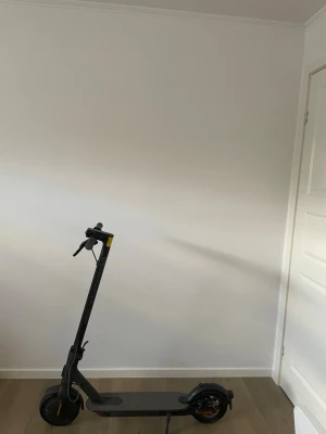 Svart elscooter med digital display - Säljer en svart elscooter med stilren design och digital display som visar hastighet, batterinivå och Bluetooth-anslutning. Scootern har orange detaljer på hjulen och handtaget. Perfekt för smidig transport i stan.