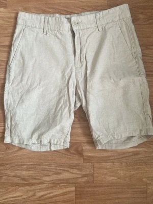 Nya och oanvända Beige shorts  - Snygga beige shorts i bomull med klassisk passform. De har två sidofickor, bälteshällor och stängs med knapp och dragkedja. Perfekta för varma dagar och enkla att matcha med olika stilar.