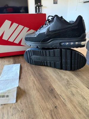 Nike Air Max svart sneakers - Snygga svarta Nike Air Max sneakers i läder och syntet med klassisk synlig Air Max-dämpning i sulan. Skorna har en låg profil, svart sula och diskret Nike-logga på sidan. Perfekta för dig som gillar stilrena och sportiga sneakers.