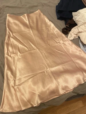 Champagnefärgad satinkjol - Snygg långkjol i skimrande champagnefärgad satin. Kjolen har en lätt utsvängd form och slät midja, perfekt för en trendig och elegant look. Passar till både sneakers och klackar.