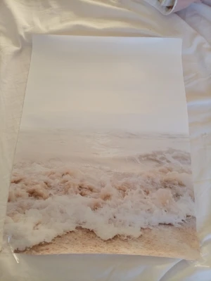 Poster med strandmotiv i beige toner - Säljer en poster med ett lugnt strandmotiv där vågor slår in mot sanden. Färgerna går i mjuka beige och vita nyanser, vilket ger en harmonisk känsla. Tryckt på papper och passar perfekt som väggdekoration i sovrum eller vardagsrum. 30X40cm 