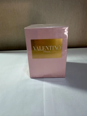 Valentino Donna Eau de Parfum 100ml - Lyxig parfym från Valentino i serien Donna. Förpackningen är ljusrosa med en elegant guldfärgad etikett framtill. Flaskan rymmer 100 ml och är perfekt för dig som gillar exklusiva dofter och snygg design.