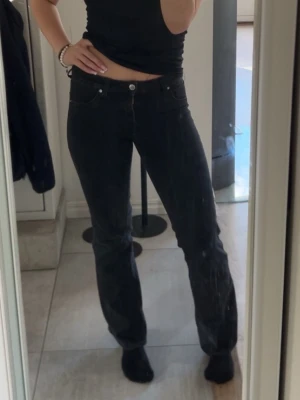 Svarta raka jeans med ganska låg midja - Säljer ett par svarta jeans med raka ben och ganska låg midja. Jeansen har klassisk femficksdesign och stängs med knapp och dragkedja. Perfekta till en avslappnad och trendig stil.