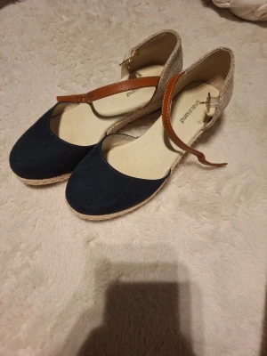 Blå espadrillesandaler från Gioseppo -  Storlek 32 men kan passa 33-34. Snygga espadrillesandaler från Gioseppo med blå textil framtill, beige häl i grovt tyg och bruna remmar i läderimitation. Sandalerna har klassisk flätad sula i jute och öppen design med justerbart spänne runt vristen. Perfekta för sommaren!