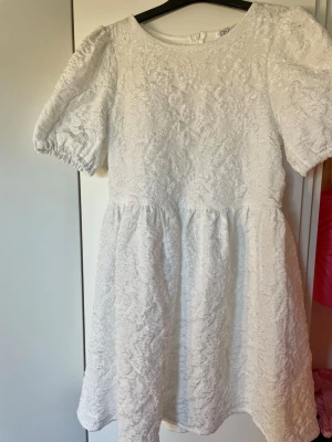 Vit kort klänning med puffärm - Supersöt vit kort klänning med puffärmar och rund hals. Klänningen har ett vackert material med struktur och ett fint mönster. Perfekt för dig som ska ta studenten, passar även många andra olika tillfällen💕HELT NY! Och slutsåld!!
