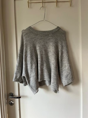 Grå stickad tröja - Mysig grå stickad tröja med oversized passform och vida ärmar. Tröjan har rund halsringning och är tillverkad i ett mjukt, melerat garn. Perfekt för lager-på-lager och chill dagar. Obs har klippt den själv 