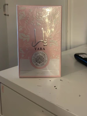 Yara parfym från Lattafa - Yara parfym från Lattafa i en snygg rosa kartong med blommigt mönster och silverdetaljer. Parfymen är tillverkad i Förenade Arabemiraten och kommer i en elegant förpackning som känns lyxig och modern.