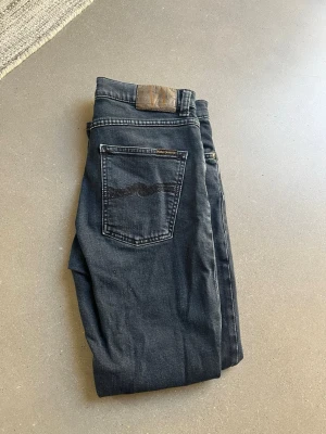 Mörkblåa jeans från Nudie  - Snygga mörkblåa jeans från Nudie Jeans med klassisk femficksdesign och diskret vågmönster på bakfickan. Jeansen har raka ben och är tillverkade i mjukt denimtyg. Storleken är w28 l30 men bredden på jeansen är större så dem sitter ungefär som ett par 29or. Hör av er vid minsta fundering.