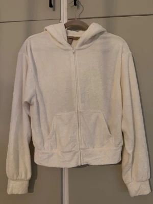 Vit zip-hoodie från H&M i frotté - Mysig vit hoodie från H&M i frottéliknande material. Tröjan har dragkedja framtill, två fickor och en stor huva. Perfekt för en avslappnad och chill stil. Långa ärmar med muddar och avslappnad passform. Endast testad men ej använd. 