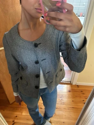 Grå jacka från Flare Collection - Snygg grå kappa från Flare Collection med rund halsringning och stora svarta knappar framtill. Jackan har en trendig look och perfekt att styla med jeans. Står ingen storlek men skulle säga att de är en storlek S. Godkänner prisförslag vid snabb affär!💕