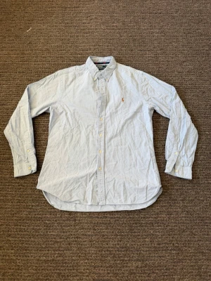 Ralph Lauren skjorta - Klassisk ljusblå skjorta från Ralph Lauren med button-down krage och broderad logga på bröstet. Passar både M/L. Skjortan har långa ärmar, knappar framtill och är tillverkad i mjuk bomull. Perfekt till en clean och stilren look.