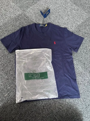 Mörkblå t-shirt från Polo Ralph Lauren - Mörkblå t-shirt från Polo Ralph Lauren med klassisk röd broderad logga på bröstet. T-shirten har rund halsringning och är tillverkad i mjuk bomull. Perfekt för en stilren och avslappnad look. M/S