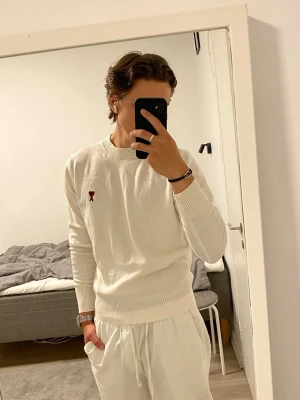 Ami Paris tröja - Säljer en stilren vit tröja från Ami Paris med det ikoniska röda hjärtat broderat på bröstet. Tröjan har rund halsringning, långa ärmar och ribbade muddar. Perfekt för en clean och trendig look. Storlek M men liten i storleken. Jag är 177cm