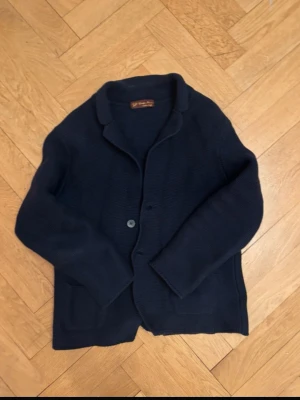 Mörkblå cardigan från Giuseppe Ferrarino - Snygg mörkblå cardiganjacka i storlek S från Giuseppe Ferrarino, tillverkad i Italien. Jackan är stickad med två knappar framtill, har krage och två fickor. Perfekt för lager-på-lager och en stilren look.