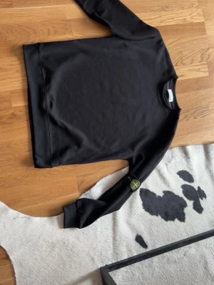 Svart sweatshirt från Stone Island - Svart långärmad sweatshirt från Stone Island med klassisk rund hals och ikonisk logotyp-patch på ärmen. Tröjan har en stilren design och är tillverkad i mjuk bomull för maximal komfort.