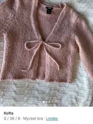 Rosa fluffig kofta från Lindex - Supersöt rosa kofta från Lindex i fluffigt material. Modell med långa ärmar och knytband framtill. Perfekt att slänga över en topp för en mysig och trendig look. Djup v-ringning och mjuk känsla.