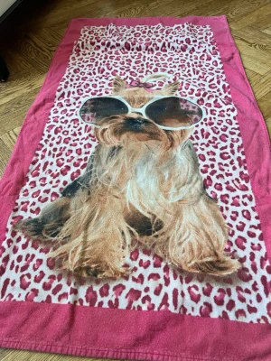Strandhandduk med hund och leopardmönster - Cool strandhandduk i rosa med leopardmönster och en stor bild av en hund med solglasögon. Perfekt för stranden eller poolen, handduken är mjuk och har en färgstark design som sticker ut. Materialet är bomullsfrotté.