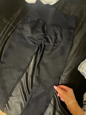 Svarta scrunch leggings med hög midja - Snygga svarta leggings med scrunch-detalj bak och hög midja. Sömlös design och stretchigt material som formar sig efter kroppen. Perfekta för gymmet eller chill hemma. Mjukt och bekvämt tyg.