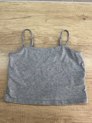 Grå croppad linnetopp - En enkel och stilren grå croppad linnetopp med smala axelband. Perfekt att matcha med jeans eller kjol för en avslappnad look. Mjuk och stretchig känsla. Lager 157 storlek:M