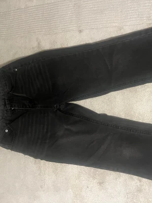 Svarta raka jeans - Säljer ett par svarta jeans med rak passform och klassisk femficksdesign. Jeansen har subtila slitningar framtill och är tillverkade i ett mjukt denimtyg. Perfekta för en avslappnad och stilren look.