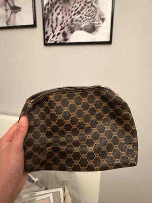  brun necessär med monogram - Snygg brun necessär med klassiskt GG-monogram i beige. Väskan har en mjuk, rundad form och dragkedja upptill. Perfekt för att förvara smink eller småprylar i väskan. Tillverkad i tåligt material med exklusiv känsla.