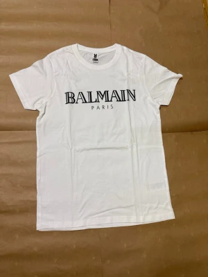 Balmain Paris t-shirt - Säljer en vit t-shirt från Balmain Paris med klassisk logga i svart på bröstet. Helt ny aldrig använd. Storlek S