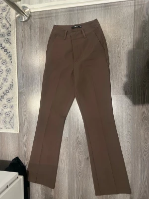Bruna kostymbyxor från BikBok - Snygga bruna kostymbyxor från BikBok med raka ben och pressveck.  Använd 1-2 gånger. Storlek 34💖