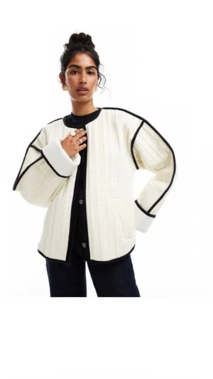 Vit quiltad jacka med svarta detaljer - Säljer en oversized vit quiltad jacka med svarta kontrastkanter och knäppning framtill. Jackan har rund halsringning, breda ärmar och en cool, boxig passform. Perfekt för lager på lager och ger en trendig look. Aldrig använd fortfarande i plasten. 