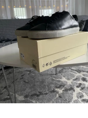 Svarta låga sneakers i läder - Stilrena svarta sneakers i slätt läder med vita sulor och klassisk snörning. Enkel och tidlös design som passar till det mesta. Perfekta för dig som gillar minimalistisk stil.